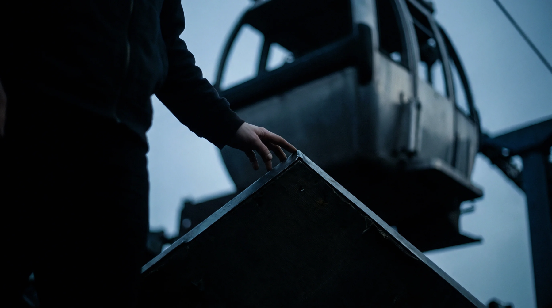 A hand rests upon the cold steel edge of a large industrial mold component within a dimly lit production facility setting.