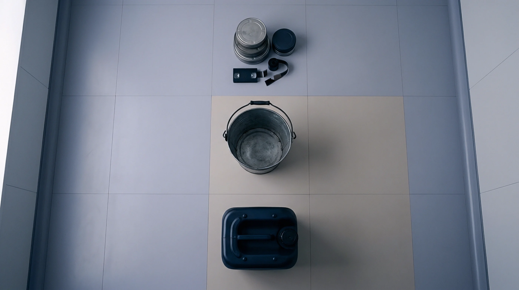 Various industrial containers including metal canisters with film strip, a steel bucket, and a molded plastic jerrycan rest on a tiled surface.