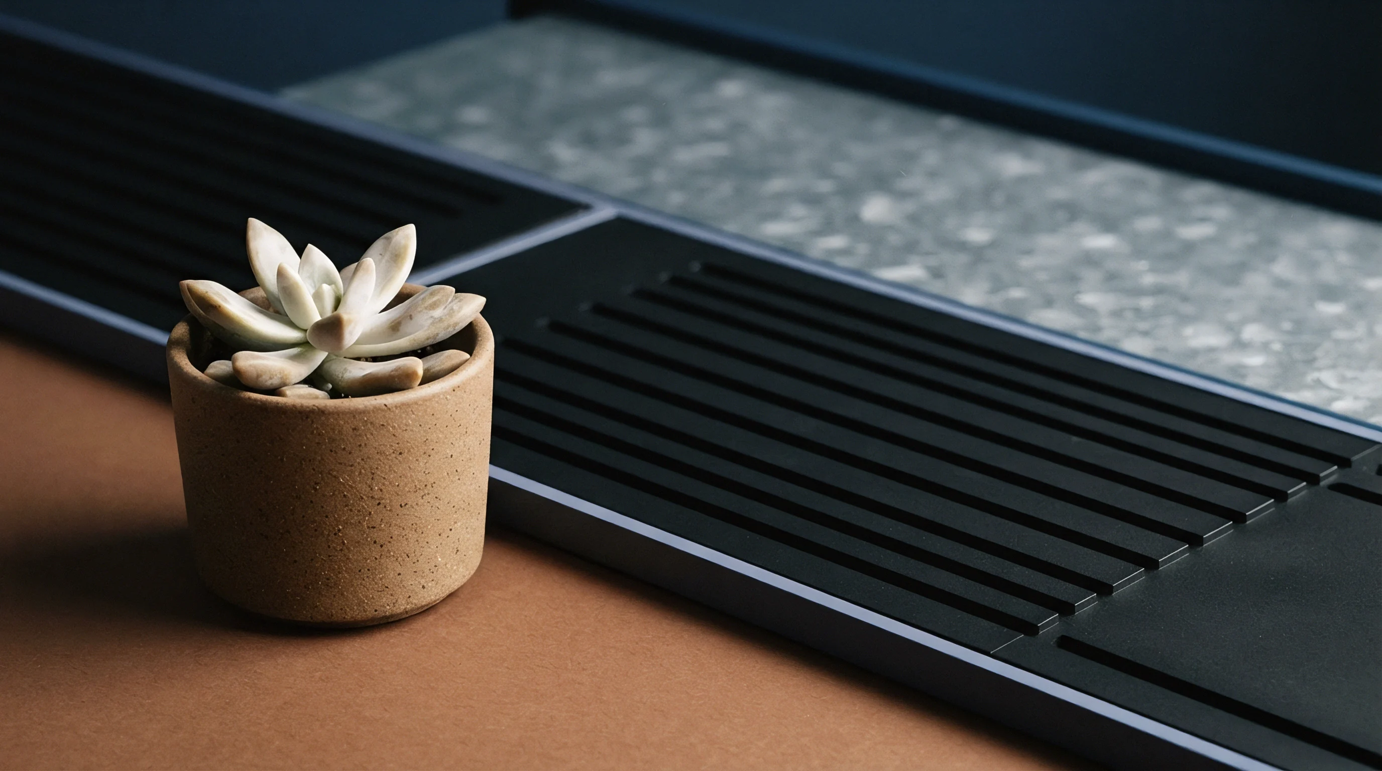 A grooved black elastomeric polymer profile sits alongside a speckled composite sheet and a small potted succulent on a brown surface.