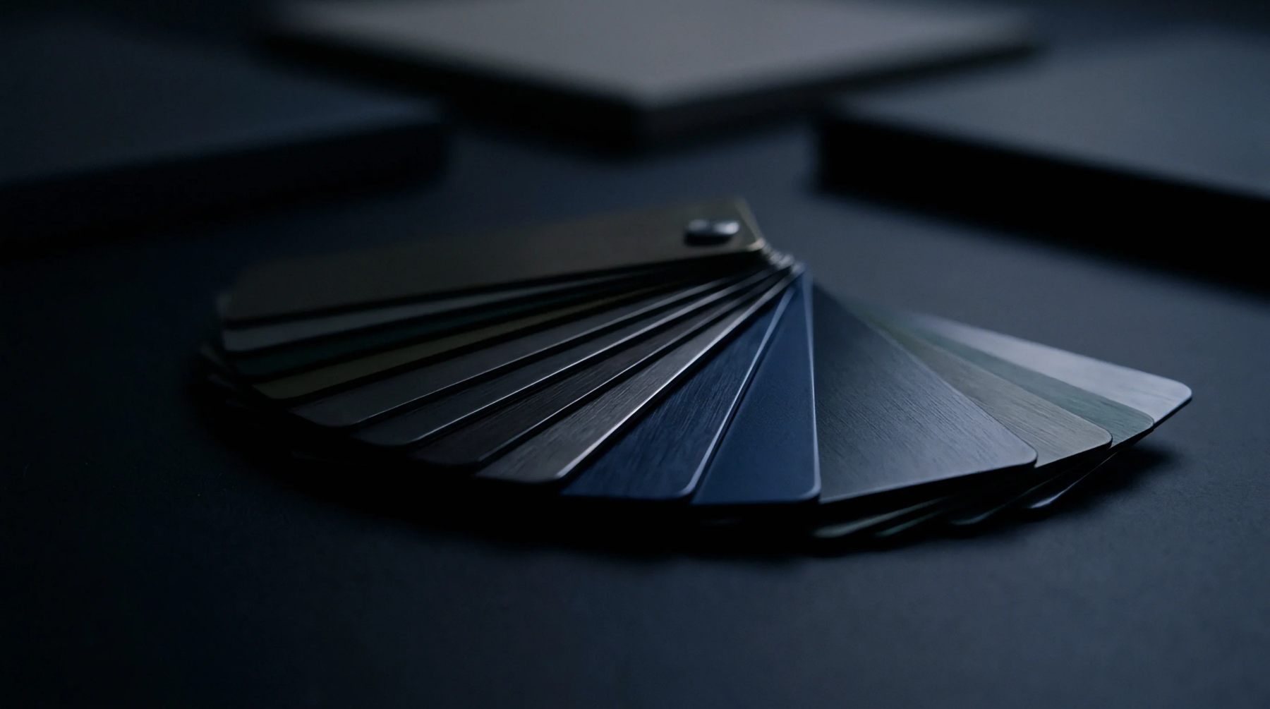 A digital render shows a set of rectangular polymer material samples with various dark metallic finishes resting on a matte surface.