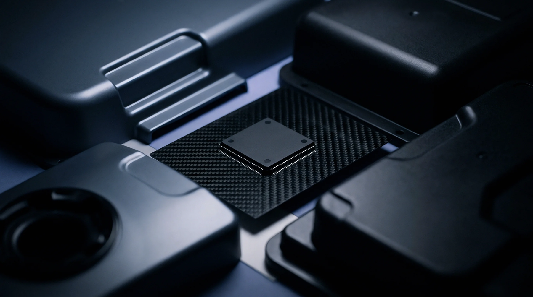 Dark injection molded polymer enclosures and a central microchip mounted on a textured carbon composite board rest on a flat surface.