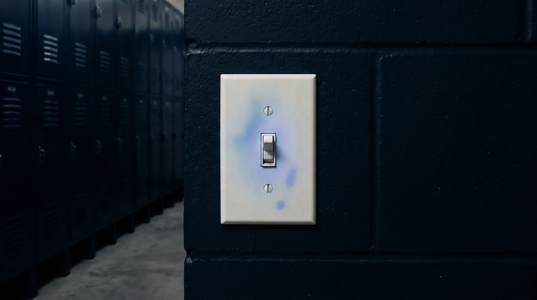 A light switch plate composed of injection moulded polymer exhibits localised discolouration and surface contamination against a dark masonry wall background.